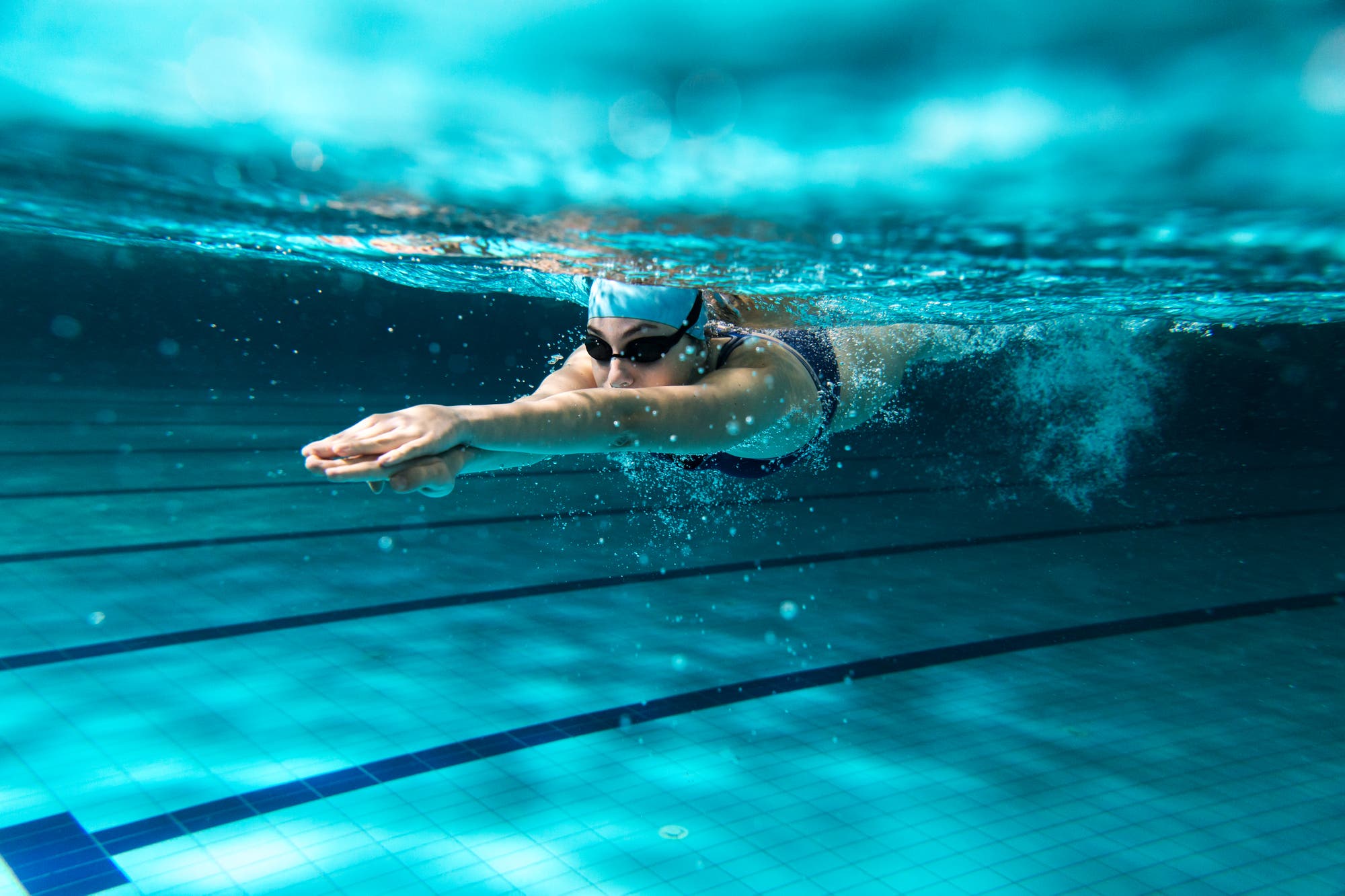 Unterwasseraufnahme einer Schwimmerin mit Badekappe und Schwimmbrille.