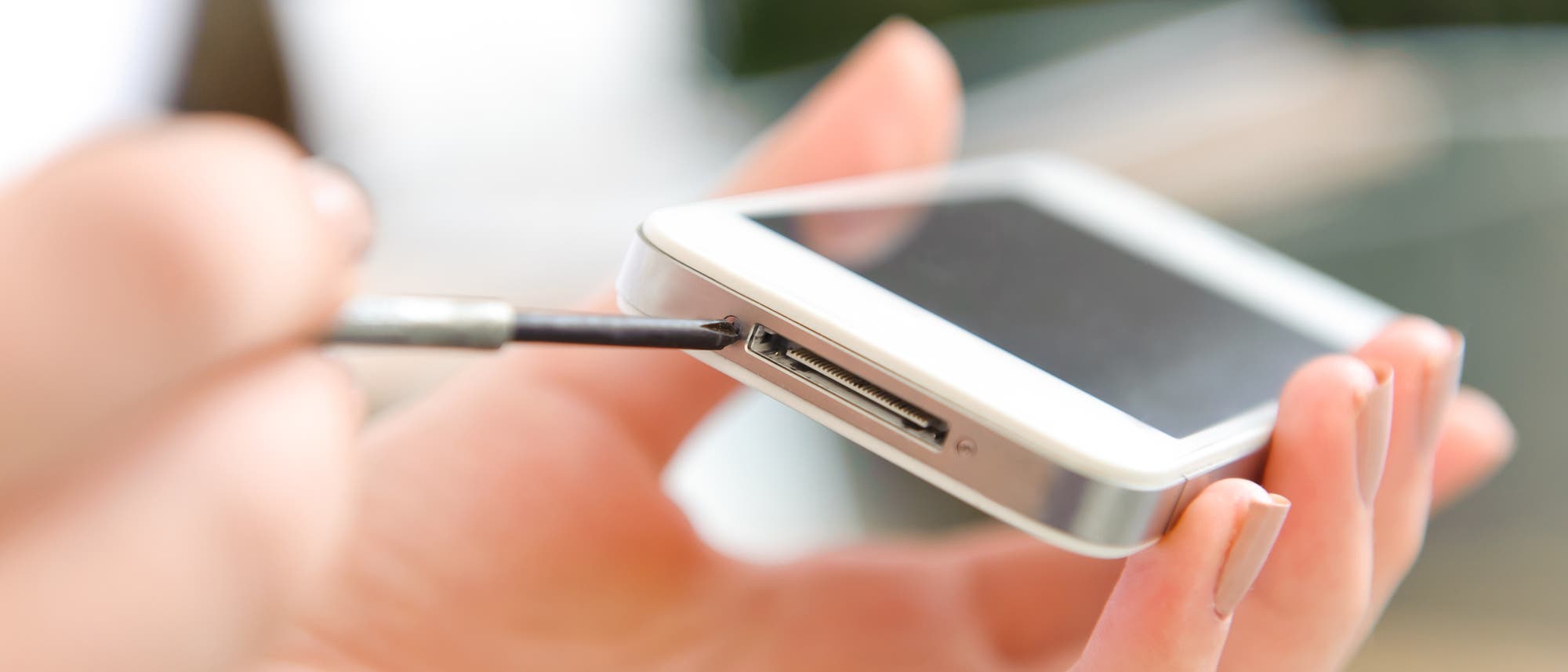 Eine Hand prökelt mit einem Schraubenzieher an einem Apple-Smartphone herum. Eine Hand prökelt mit einem Schraubenzieher an einem Apple-Smartphone herum.