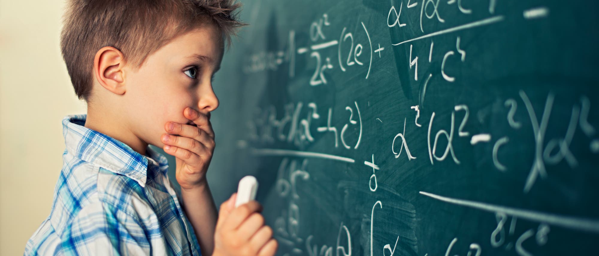 Ein Junge in einem karierten Hemd steht nachdenklich vor einer Tafel, die mit komplexen mathematischen Formeln beschrieben ist. Er hält ein Stück Kreide in der Hand und scheint über die Lösung nachzudenken. Die Szene vermittelt ein Gefühl von Konzentration und Lernen. Ein Junge in einem karierten Hemd steht nachdenklich vor einer Tafel, die mit komplexen mathematischen Formeln beschrieben ist. Er hält ein Stück Kreide in der Hand und scheint über die Lösung nachzudenken. Die Szene vermittelt ein Gefühl von Konzentration und Lernen.