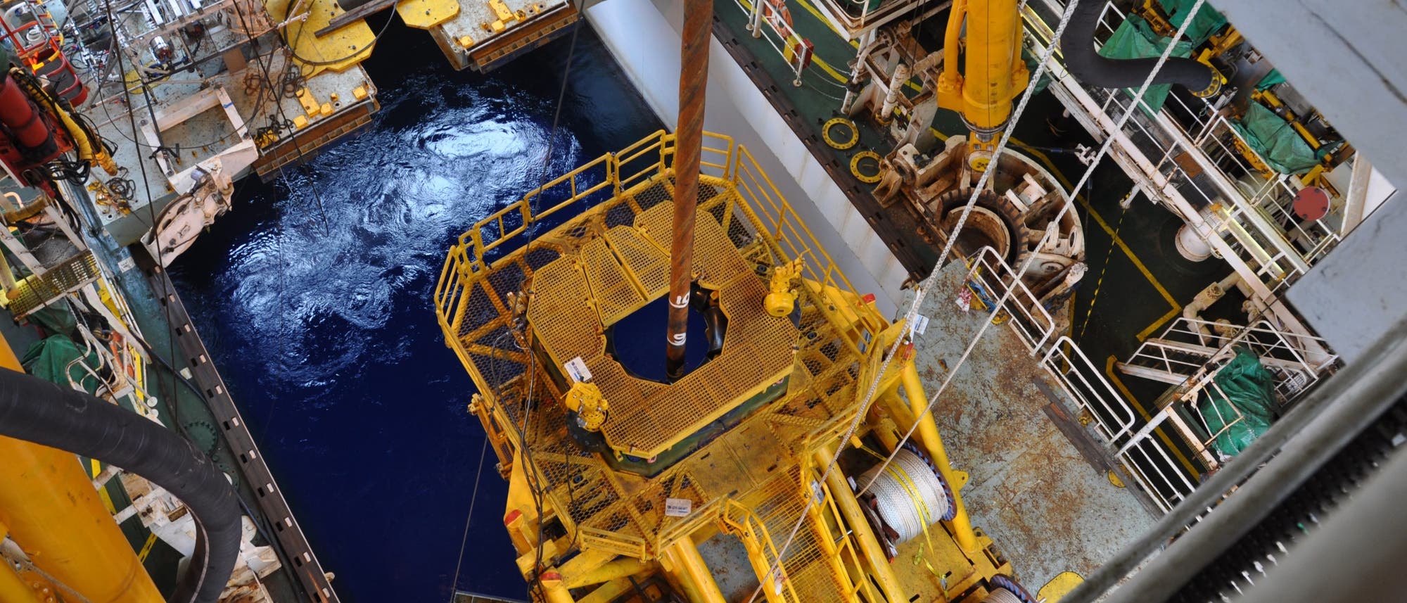 Blick in den Bohrschacht des Bohrschiffes Chikyu mit Bohrer, der zur Wasseroberfläche hinabgelassen wird. Blick in den Bohrschacht des Bohrschiffes Chikyu mit Bohrer, der zur Wasseroberfläche hinabgelassen wird.