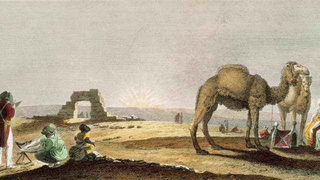 Eine historische Illustration zeigt eine Wüstenlandschaft bei Sonnenaufgang. Im Vordergrund stehen zwei Kamele, neben denen zwei Personen in traditionellen Gewändern sitzen. Links sind weitere Personen zu sehen, darunter eine Person, die auf einer Staffelei malt. Im Hintergrund ist eine Ruine zu erkennen. Die Szene vermittelt eine ruhige, historische Atmosphäre in einer Wüstenumgebung.