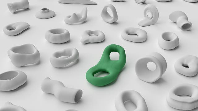 Eine Sammlung von abstrakten, weißen, organisch geformten Objekten, die auf einer ebenen Fläche verteilt sind. In der Mitte hebt sich ein einzelnes, grünes Objekt hervor, das sich durch seine geschwungene Form und zwei Öffnungen von den anderen unterscheidet. Die Anordnung der Objekte erzeugt ein Gefühl von Vielfalt und Individualität innerhalb einer homogenen Gruppe.