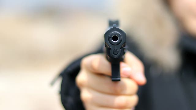Blick in den Lauf einer Schusswaffe, die eine Person auf den Betrachter hält.