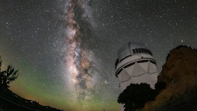Ein großes Teleskop steht unter einem klaren Nachthimmel, der von der Milchstraße durchzogen ist. Die Sterne leuchten hell, und die Galaxie erstreckt sich vertikal über das Bild. Rechts im Vordergrund ist das Teleskop sichtbar, während links Bäume und Felsen zu sehen sind. Die Szene vermittelt die Ruhe und Majestät des Universums.