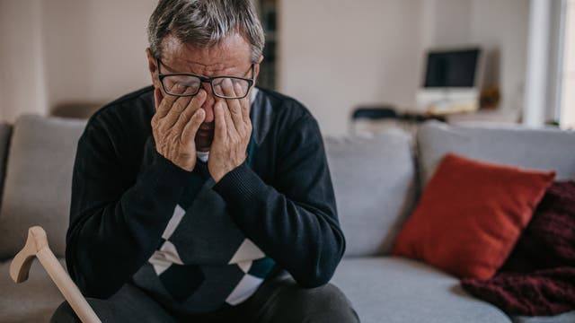 Älterer Mann sitzt auf Bett und reibt sich die Augen