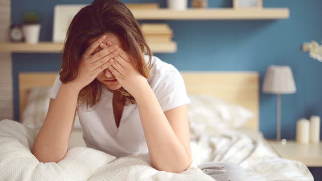 Frau sitzt im Bett, stützt sich auf die Ellbogen und hält die Hände vors Gesicht.