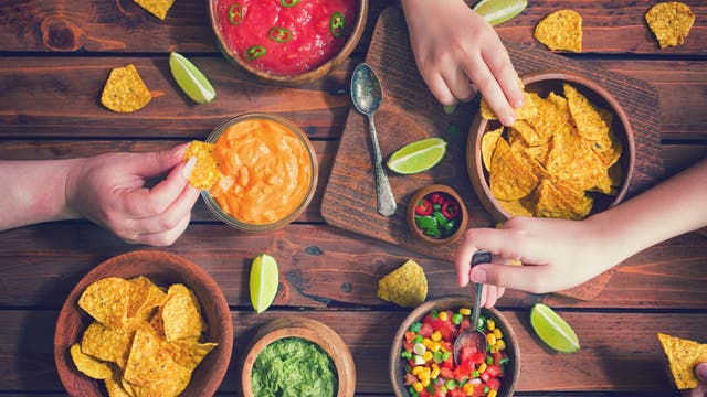 Drei Hände greifen nach Snacks auf einem Tisch