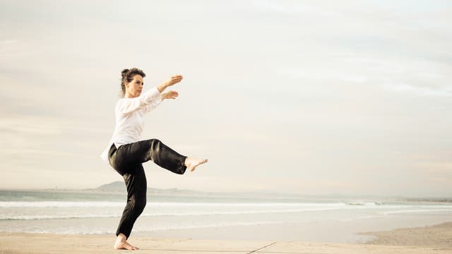 Frau macht Tai Chi auf einem Steg am Meer